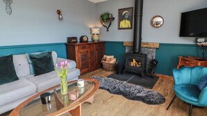 Ein Wohnzimmer mit einer Couch, einem Glastisch, einem blauen Sessel, einem Kamin und einem Fernseher.