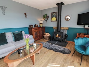 A living room with a sofa, a glass coffee table, a blue armchair, a fireplace, and a television. - Crown Cottage (Dunfermline)