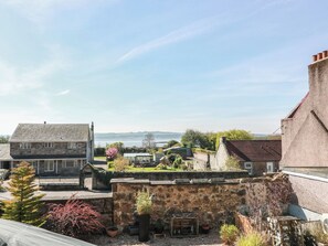 A stone building with a small garden, a view of the sea, and a clear sky. - Crown Cottage (Dunfermline)