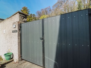 A gated entrance with a metal door, a stone wall, and a small green planter. - Crown Cottage (Dunfermline)