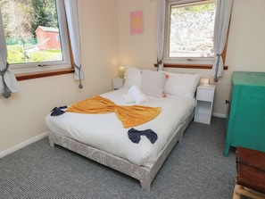 A bedroom with a bed, two bedside tables, a nightstand, a green cabinet, and a window with curtains.