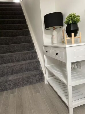 A staircase with carpeted steps, a white desk with drawers, a lamp, a small plant, and a bottle. - St Andrews Golf Getaway - 3.5 miles to Old Course + Private Putting Green (St Andrews)