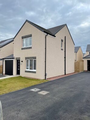 A modern two-story house with a garage, a well-maintained lawn, and a paved driveway. - St Andrews Golf Getaway - 3.5 miles to Old Course + Private Putting Green (St Andrews)