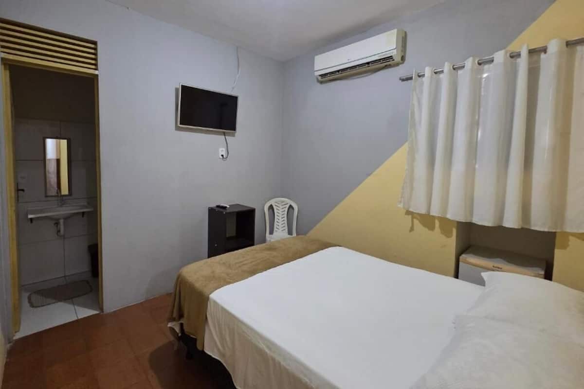 A bedroom with a bed, a TV, an air conditioner, and a shower area.