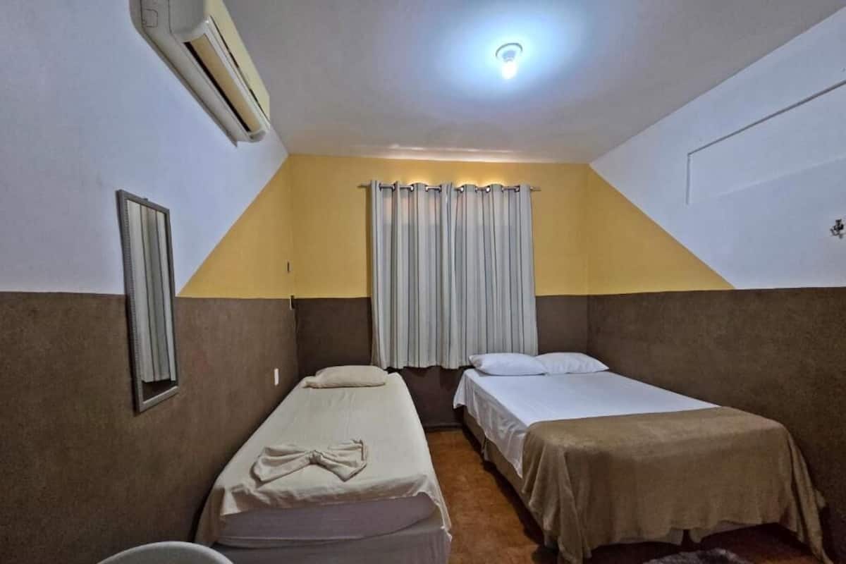 A room with two beds, a ceiling fan, a window with curtains, and a small rug.