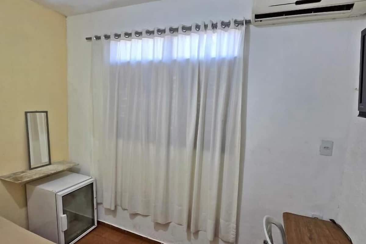 A room with a bed, a small desk, a chair, a mirror, and a window with curtains.