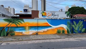 A colorful mural on a building with palm trees, a sunset, and ocean waves. - Pousada SolMaris (João Pessoa)