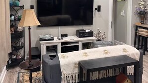 A living room with a flat-screen TV, a sofa, a lamp, a coffee table, and a bookshelf.