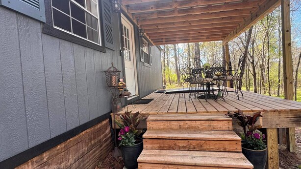 A wooden deck with steps leading to a covered porch, a metal bench, and a lantern.