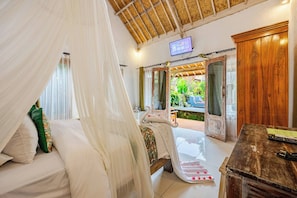 A room with a bed under a canopy, a wooden desk, and a television on the wall.