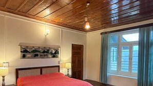Una habitación con techo de madera, una cama con una colcha roja, un tapete estampado, una obra de arte en la pared y una ventana con cortinas.