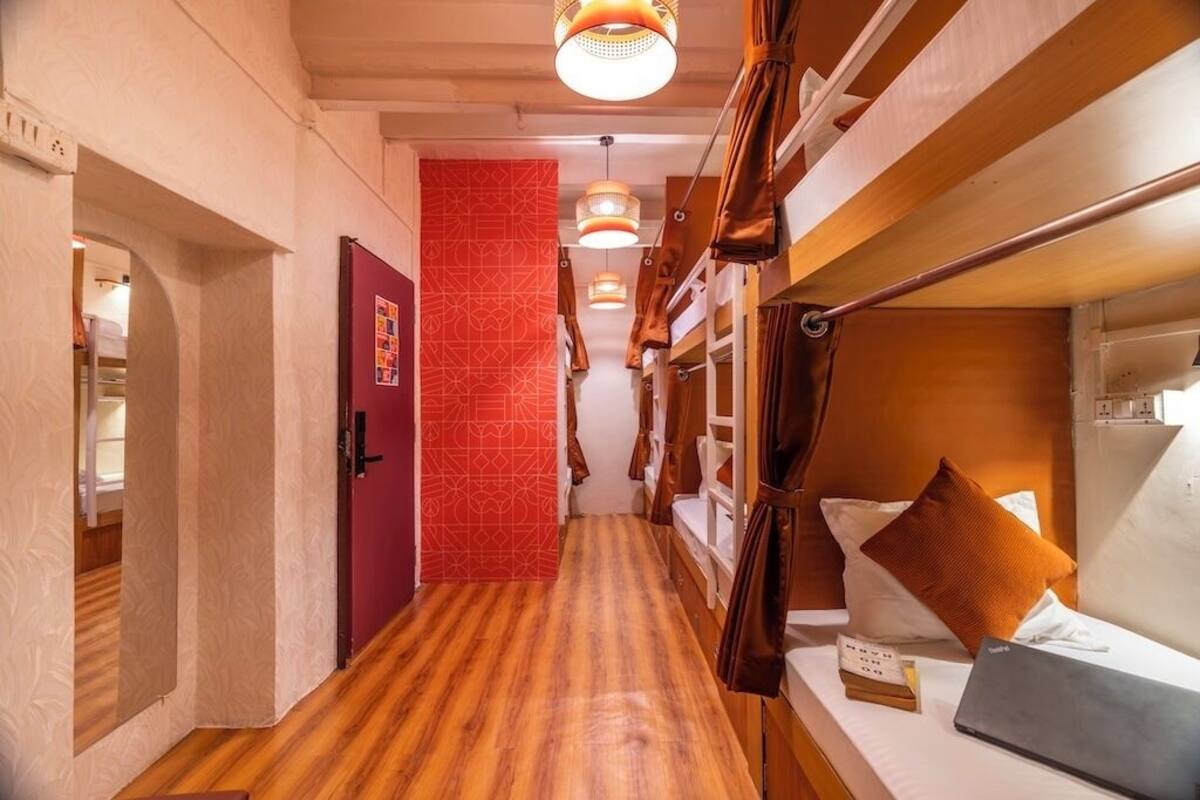 Un pasillo estrecho con literas, una puerta roja y luces colgantes.