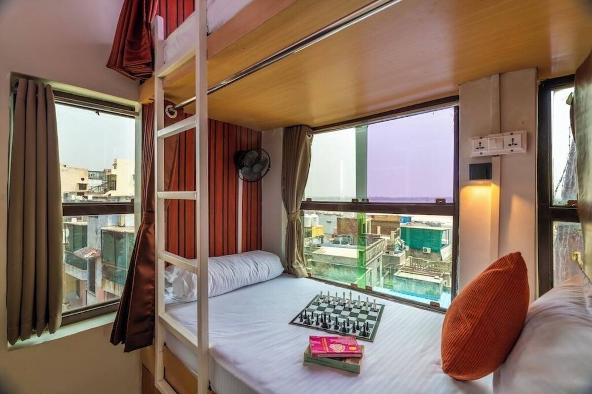 Habitación con literas, un tablero de ajedrez, una ventana con cortinas y vista a la ciudad.