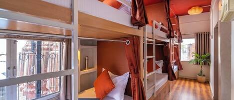 A bunk bed room with a window, a plant, and a wooden floor.