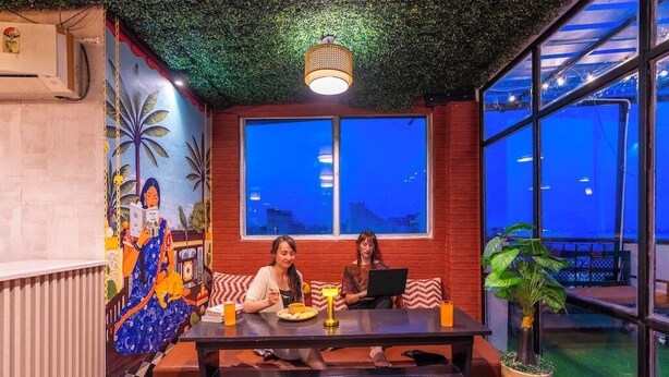 A room with a mural, a table with two people, a laptop, and a plant.