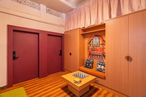 A room with two red doors, a wooden cabinet with a colorful tapestry, and a chessboard on a small table.