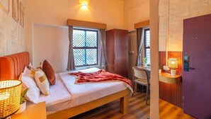 A hotel room with a bed, a desk, a chair, a window with curtains, and a door.