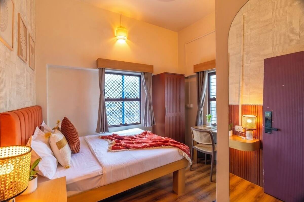 Una habitación de hotel con cama, escritorio, silla, ventana con cortinas y puerta.