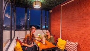 A room with a brick wall, a wooden table, and a window with a view of a cityscape at night.