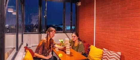 A room with a brick wall, a wooden table, and a window with a view of a cityscape at night.