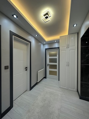 A hallway with a white door, a white cabinet, a radiator, and a black marble wall.