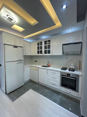 A modern kitchen with white cabinets, a Bosch refrigerator, a dishwasher, a sink, a stove, and an oven.