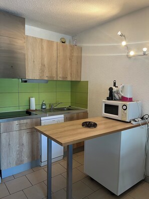 Eine kleine Küche mit einer Holz Arbeitsplatte, einer Mikrowelle, einem Spülbecken und einer grünen Rückwand.