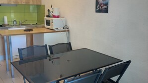 Et lille køkken med mikrobølgeovn, elkedel og vask. Spisebord med stole og et billede på væggen.
