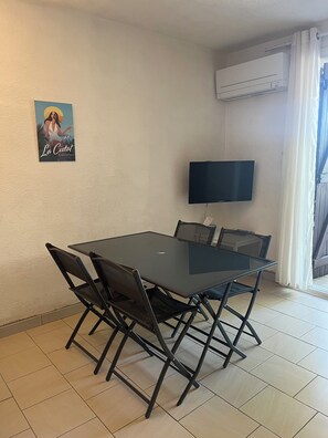 Ein Essbereich mit Tischplatte aus Glas und klappstühlen, einer Klimaanlage und einem Poster an der Wand.