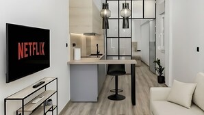 Una sala de estar moderna con un televisor de pantalla plana, un comedor con cocina al fondo y un sofá.