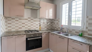 Una cucina con armadietti rosa, un piano cottura a gas, un lavello e una finestra con persiane.