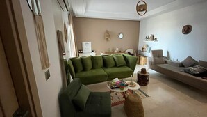 Un soggiorno con un divano verde, una poltrona verde più piccola, un tavolino rotondo con un cesto in vimini e un divano beige.