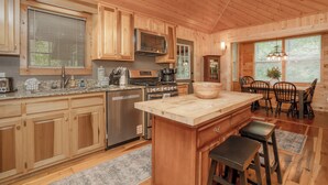 Uma cozinha rústica estilo cabana, com ilha central, eletrodomésticos embutidos e área de jantar com mesa e cadeiras de madeira.