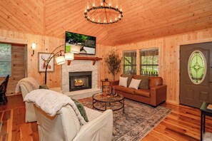 A log cabin interior with a fireplace, a sofa, a coffee table, and a chandelier. - BlueMoonOL: HotTub*Wifi*Pet-Friendly*Yard*FirePit*Games (Sevierville)
