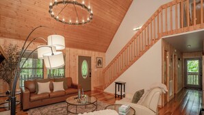 Interior de madeira com escada, sofá, mesa de centro e porta com janela de vidro verde.
