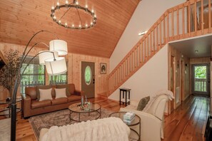 A wooden interior with a staircase, a sofa, a coffee table, and a door with a green glass window. - BlueMoonOL: HotTub*Wifi*Pet-Friendly*Yard*FirePit*Games (Sevierville)