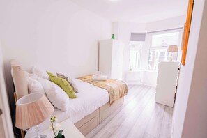 Ein Schlafzimmer mit Bett, Nachttisch, Lampe und Fenster.