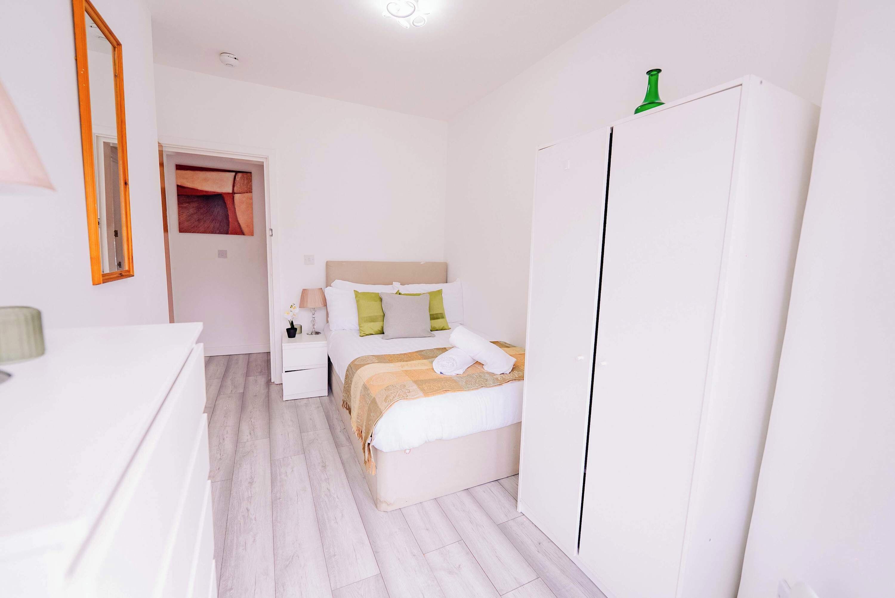 A bedroom with a bed, a wardrobe, a nightstand, and a mirror.