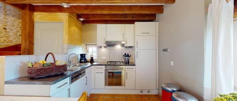 A compact kitchen with white cabinets, a gas stove, a sink, and a small trash bin.