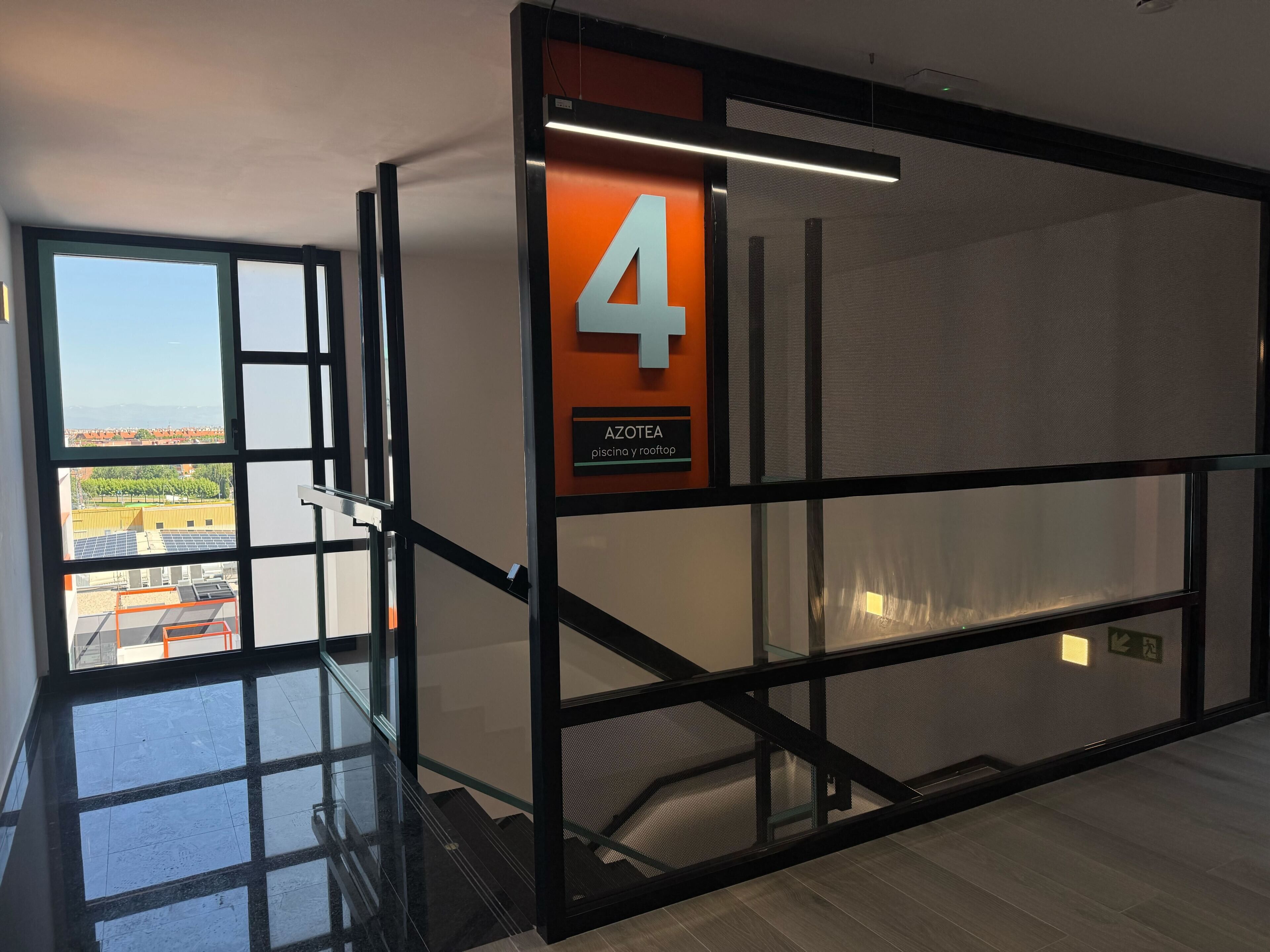 A modern interior with a glass staircase, a sign indicating room number 4, and a view of the outside.