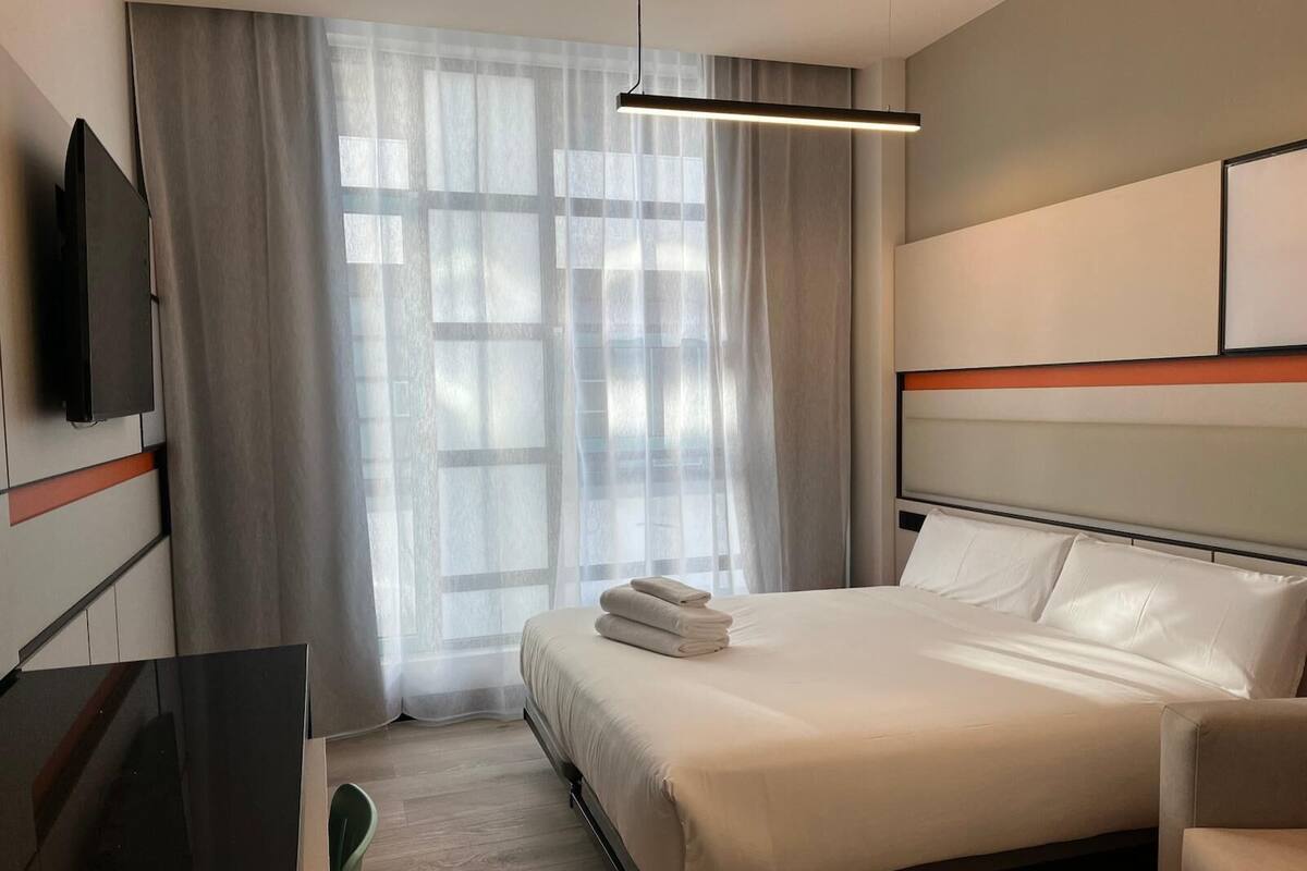 Ein Hotelzimmer mit einem Bett, einem an der Wand montierten Fernseher, einem Schreibtisch und einem Stuhl.