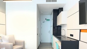 A modern hotel room with a bed, a sofa, a kitchenette, and a bathroom.