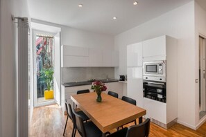 A modern kitchen with white cabinets, a wooden dining table, and a potted plant. - Luxury Stay in the Historic Center with Balcony, Wi-Fi, and Air Conditioning (Napoli)