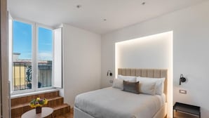Ein Schlafzimmer mit einem großen Bett, einem kleinen Tisch mit Blumen, einem Fenster mit Aussicht und einem Nachttisch.