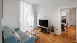 Ein modernes Wohnzimmer mit Sofa, Fernseher, Couchtisch und einem Essbereich mit Tisch und Stühlen.