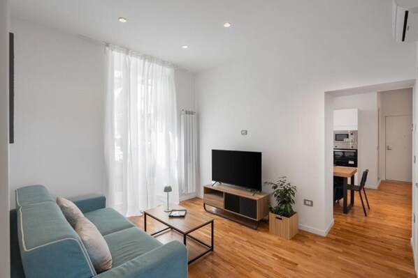 A modern living room with a sofa, TV, coffee table, and a dining area with a table and chairs. - Luxury Stay in the Historic Center with Balcony, Wi-Fi, and Air Conditioning (Napoli)