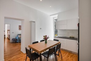 A modern kitchen with white cabinets, a wooden dining table with chairs, and a vase of flowers. - Luxury Stay in the Historic Center with Balcony, Wi-Fi, and Air Conditioning (Napoli)