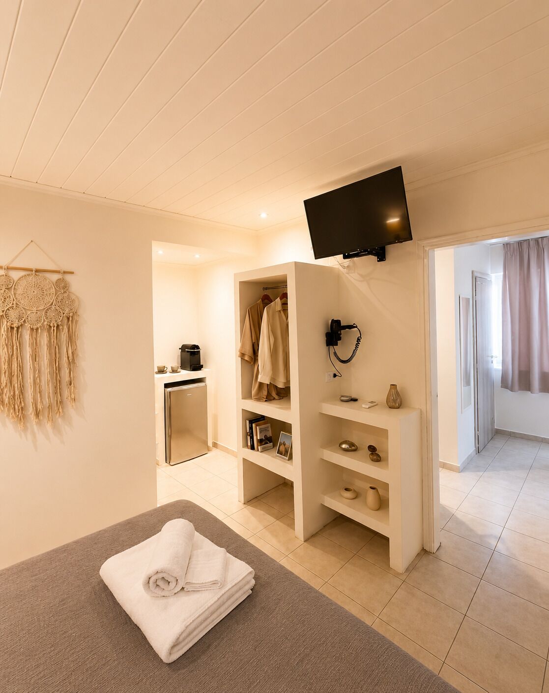 A hotel room with a bed, a TV mounted on the wall, a wardrobe, and a small kitchenette.