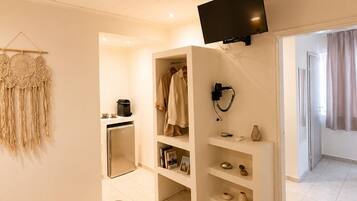A hotel room with a bed, a TV mounted on the wall, a wardrobe, and a small kitchenette.