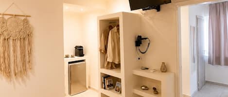 Ein Hotelzimmer mit Bett, Wandfernseher, Kleiderschrank und einer kleinen Küchenzeile.